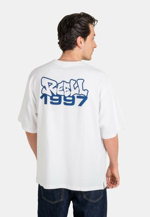 White cotton t-shirt featuring a blue graffiti-style print saying "REELL 1997" on the back. Loose fit and short sleeves.