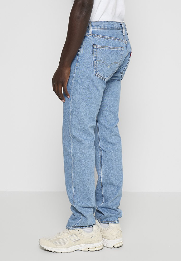 Vaqueros de denim azul claro con corte recto, diseño de cinco bolsillos y detalles de costura sutiles, combinados con zapatillas beige.