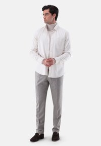 Weißes Hemd mit Knöpfen über einem beigefarbenen Rollkragenpullover, kombiniert mit grauen Hosen und dunkelbraunen Slippers. Glattes Material mit präzisen Details.