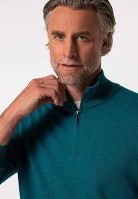 Teal zip-neck tröja med ribbad krage och muddar. Mjuk textur, tajt design och en silverdragkedja som framhävs vid halsen.