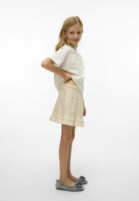 Lichtgekleurde, gestructureerde rok met een gerimpelde zoom, gecombineerd met een eenvoudige witte blouse en grijze schoenen met een decoratieve bloemenaccent.