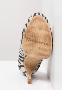 Striped high heel shoe with a soft fabric upper in black and white, showing a wooden sole with the brand name 'Tamaris' engraved.