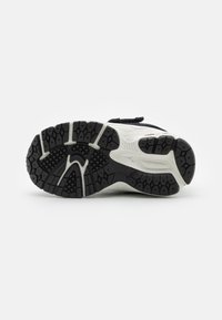 Semelle de chaussure de sport noir et blanc avec un design de semelle en caoutchouc texturé comportant des motifs hexagonaux, des canaux et des détails de soutien de la voûte.
