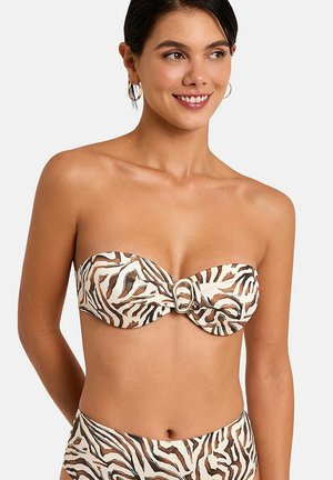 Femme souriante portant un bikini bustier avec un imprimé animal beige, marron et blanc, et un détail boucle dorée sur le haut.