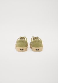 Grønne suedésneakers med lav profil, rund tå, kontrasterende beige gummisål og hvide syninger bagpå.