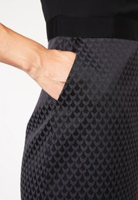 Robe noire avec une partie inférieure texturée de couleur gris foncé comportant un tissu à motifs. Comprend une poche, avec une taille lisse au-dessus.