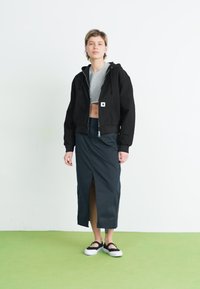 Fekete, cropped kapucnis pulóver elülső cipzárral, alatta szürke cropped top, hosszú navy szoknya hasítékkal, és fekete szandál fehér talppal.