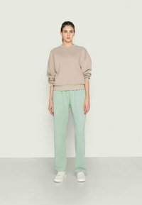 Sweatshirt bege com decote redondo e ombros caídos, combinado com calças largas de um verde menta claro e ténis brancos.