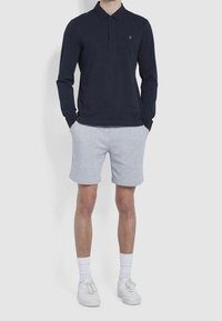 Námořnická polo košile s dlouhým rukávem, límečkem a logem, kombinována se šedými šortkami. Doplněno bílými teniskami a bílými ponožkami po kotníky.