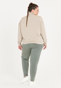 Beige långärmad pullover och gröna avsmalnande byxor med en mjuk textur. Outfitten kompletteras med vita avslappnade skor.