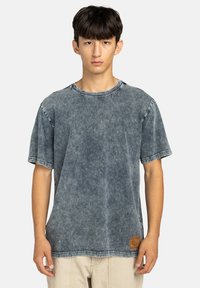 Denim t-shirt in een vervaagde blauwe kleur, met een ronde hals, korte mouwen, zichtbare stiksels en een rechthoekige logopatch op de onderste zoom.