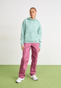 Moletão verde claro com um bolso frontal, combinado com calças rosas e ténis brancos. O conjunto tem um corte descontraído e um design simples.