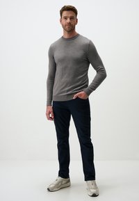 Un pull gris à manches longues avec un col rond, associé à un pantalon bleu foncé et des baskets claires, présenté sur un fond neutre.