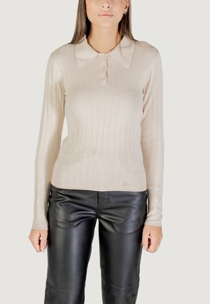 Maglione a maniche lunghe beige a coste con colletto e tre bottoni. Abbinato a pantaloni in pelle nera, che evidenziano i contrasti di texture.