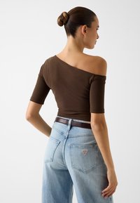 Brązowy prążkowany top z odkrytymi ramionami i krótkimi rękawami, zestawiony z jasnoniebieskimi, luźnymi jeansami z naszywką z logo na tylnej kieszonce.