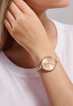 Roségoldene Armbanduhr mit rundem Ziffernblatt, strukturiertem goldenen Ziffernblatt und Kristallakzenten. Sie verfügt über ein verlinktes Metallband und ein minimalistisches Design.