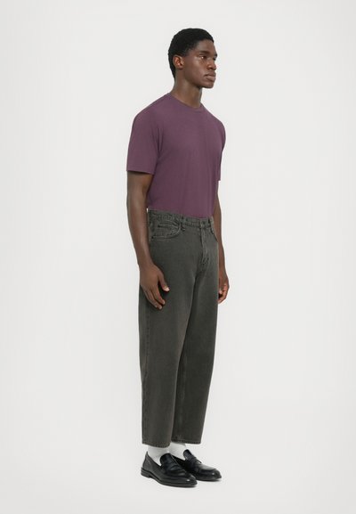 Lila kortärmad t-shirt för män kombinerad med mörkgrå, löst sittande jeans. Svarta loafers och vita strumpor fulländar outfiten. Enkel design.