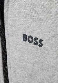Šedá mikina vyrobená z texturované látky s černým gumovým logem "BOSS" na hrudi a černým zipem.