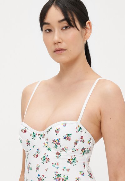 Body intimo bianco con stampa floreale, dotato di spalline sottili e decorato con fiori colorati e foglie verdi su una superficie lucida. Caratterizzato da un design aderente.