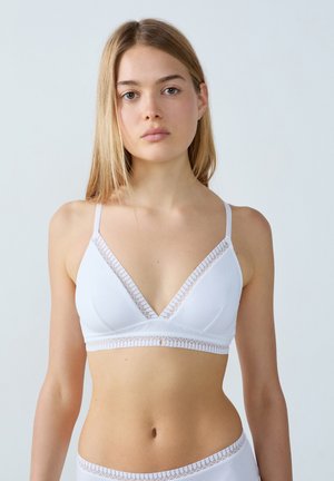 Bralette blanco en forma de triángulo con tirantes finos y borde de encaje a lo largo del escote y la parte inferior del busto; tejido suave y detalles de costura mínimos.