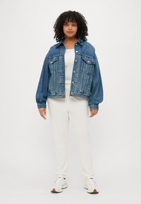 Denimsjakke med en lett oversized passform, som har to brystlommer, knappelukking og en falmet blå farge. Bæres over en hvit topp og lyse bukser.