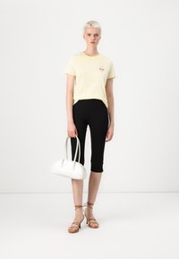 Stripet gul t-skjorte, sorte leggings og sandaler i brunt skinn med stropper. Lille broderidetalj på skjorten. Hvit håndveske med runde håndtak.