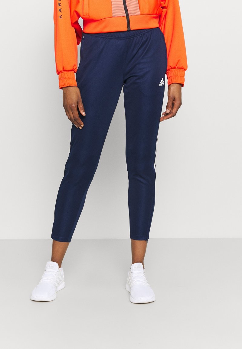 Marinblå sportleggings gjorda av stretchigt tyg, med vita sidolinjer och ett elastiskt midjeband, tillsammans med vita sneakers.