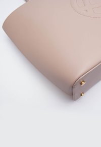 Borsa a mano in pelle rosa chiaro con una texture liscia, caratterizzata da dettagli in hardware dorato e una forma arrotondata, logo in rilievo sul davanti.
