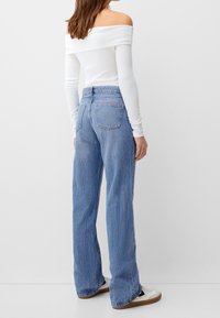 Lichtgewicht witte off-shoulder top gecombineerd met blauwe hoge taille wijde jeans, met klassieke achterzakken en een licht vervaagde afwerking.