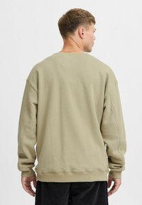 Sudadera verde oliva con un corte relajado, puños y dobladillo acanalados. Fabricada con tejido texturizado, presenta costuras de hombro caído para mayor libertad de movimiento.