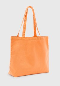 Orange canvas tote bag med två långa handtag, rektangulär form och en slät yta; har förstärkt söm vid sömmarna.