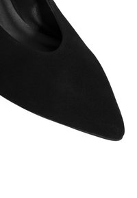 Zwarte suede pointed-toe pump met een gladde afwerking en open uitsparing aan de zijkant, met een slank silhouet en zonder zichtbare hardware.