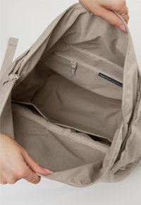 Zaino beige con un ampio scomparto interno, dotato di una tasca con zip e di un compartimento aperto. Realizzato in plastica derivante dall'impatto oceanico.