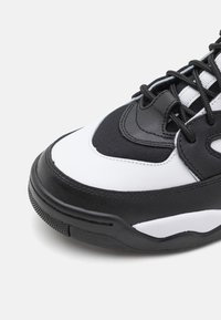Baskets noir et blanc avec une tige en cuir texturé et nylon, bout arrondi, et semelle en caoutchouc épaisse avec traction.