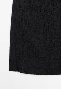 Sort tekstureret stof med subtile lodrette krusninger og en let ru overflade, vist mod en hvid baggrund.