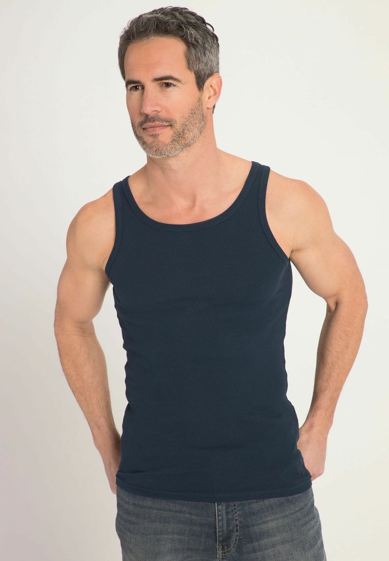 Canottiera a coste di colore blu navy con spalline larghe e forma aderente, abbinata a jeans in denim. Il materiale sembra morbido e traspirante.