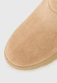Suede rudos bungas su apvaliu pirštu ir minimalistiniu dizainu. Minkšta tekstūra ir guminis padas užtikrina komfortą ir ilgaamžiškumą.