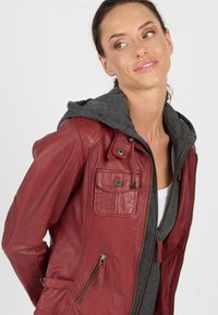 Rote Lederjacke mit grauem Hoodie-Futter, ausgestattet mit Reißverschlusstaschen, vorderen Knöpfen und einer strukturierten Oberfläche.