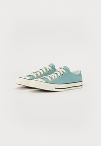 Canvas sneakers in light blue with white sole, black accent stripe, and gold eyelets. Features contrasting white laces and low-top design.