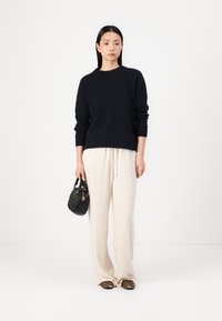 Navy sweater with long sleeves, cream wide-leg pants, black quilted handbag, and animal print slippers on a plain background.
