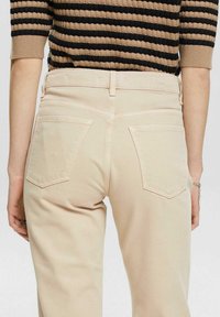 Beige denim jeans met een rechte snit, voorzien van twee achterzakken met puntige kleppen en subtiele stiksels. Glad oppervlak.