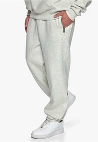Light gray sweatpants with a relaxed fit, featuring a zip pocket on the side and ribbed cuffs. Paired with white sneakers.