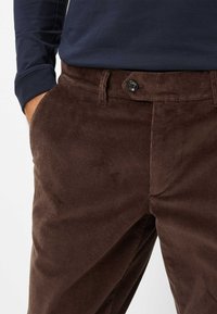 Bruine corduroy broek met een gestructureerde stof, voorzien van een knoopsluiting aan de voorkant, zijzakken en een taps toelopend ontwerp.