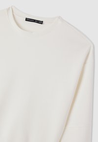 Felpa bianca con collo rotondo, maniche lunghe e texture liscia. Realizzata in un tessuto morbido, presenta un'etichetta sul collo.