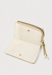 Kapsa z krémové texturované kůže otevřená, zobrazující přihrádky na karty, uzávěr na patentku a zipovou komoru se zlatým zipem a béžovými táhly.