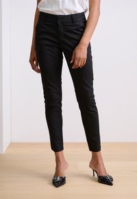 Pantalons noirs longueur cheville avec un design ajusté et un devant sans couture. Assortis à des mules noires pointues ornées d'un nœud décoratif et de quincaillerie.