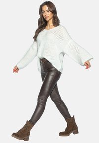 Jasnoniebieski, oversize'owy sweter dzianinowy, brązowe spodnie z ekoskóry oraz brązowe sznurowane botki na kostkę. Miękka faktura, luźny krój i wyraźne rękawy.