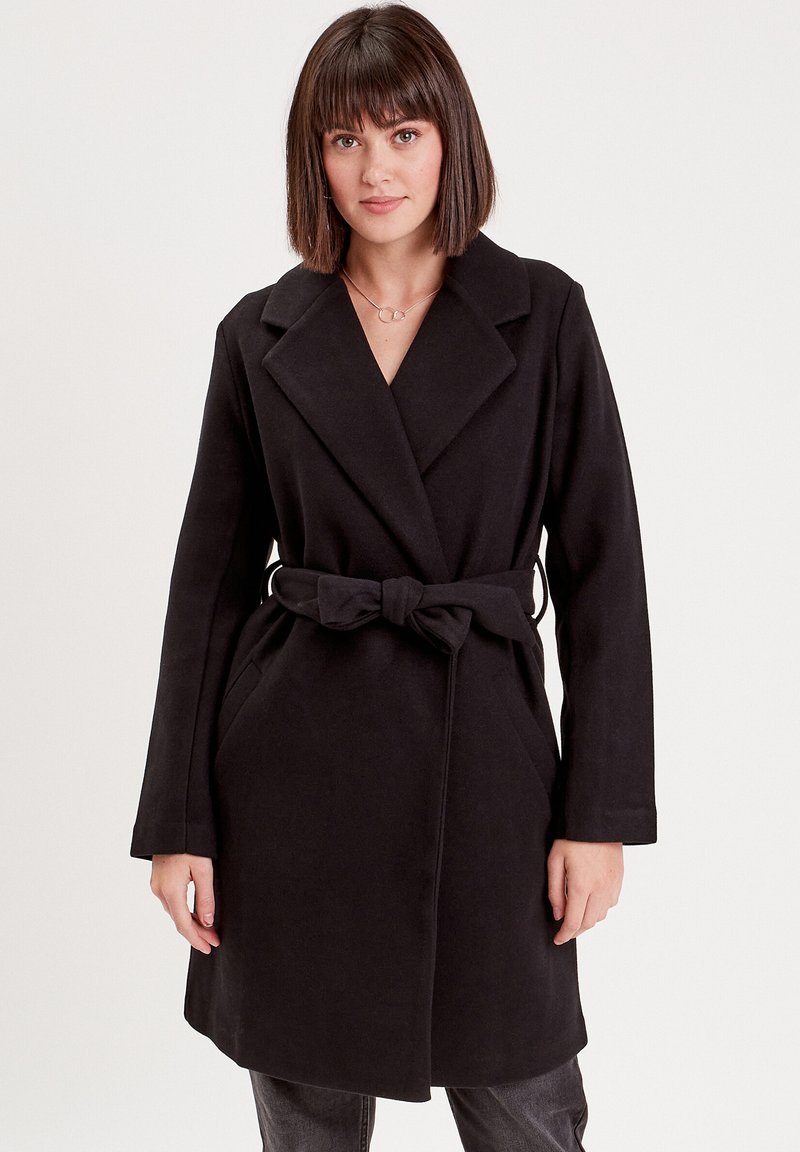 Manteau noir à ceinture avec col cranté, manches longues et poches latérales, fabriqué à partir d'un tissu doux et texturé, avec une coupe mi-longue.