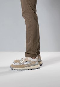 Sneaker con una combinazione di materiali beige e bianchi, tra cui suede e mesh, con una suola spessa e testurizzata e chiusura frontale con lacci.