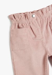 Pantalons en velours côtelé rose avec une taille froncée, fermeture à bouton argenté et une poche à patch sur le côté. Texture à côtes verticales.